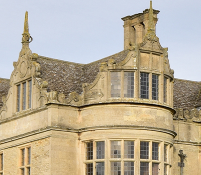 Close up of a building made of stone showing a roof and windows.